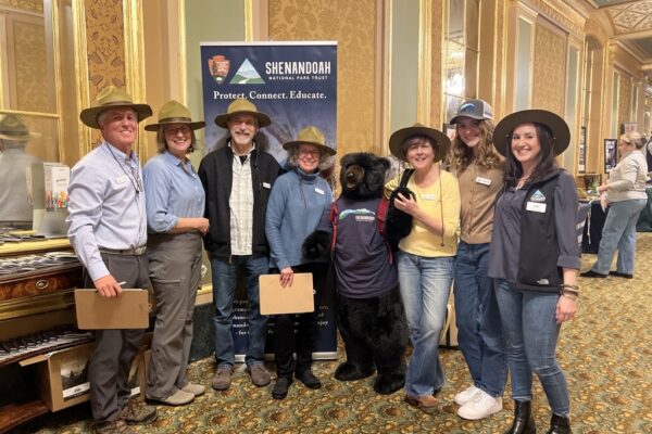 A group of volunteers in ranger hats pose with a large stuffed-animal black bear in an SNPT shirt at the Banff Film Festival.