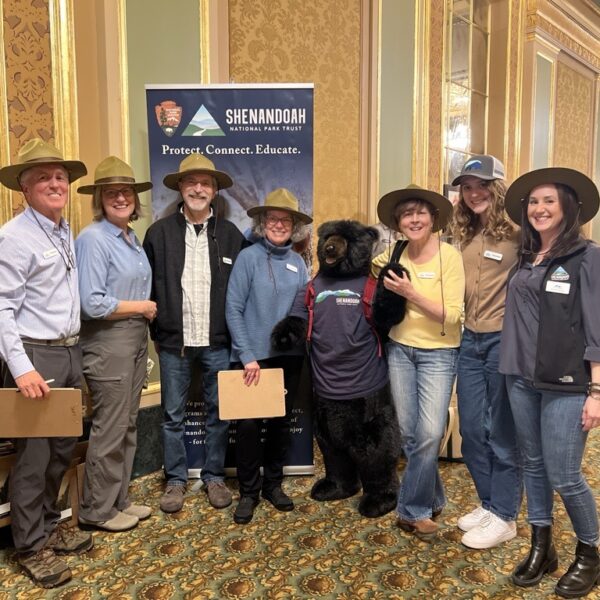 A group of volunteers in ranger hats pose with a large stuffed-animal black bear in an SNPT shirt at the Banff Film Festival.