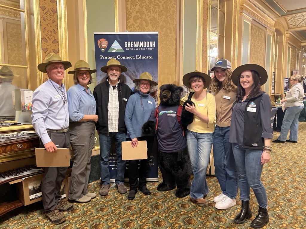 A group of volunteers in ranger hats pose with a large stuffed-animal black bear in an SNPT shirt at the Banff Film Festival.